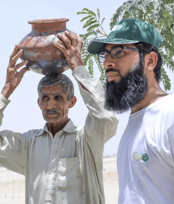 A villager carries a water pot beside a Quba volunteer